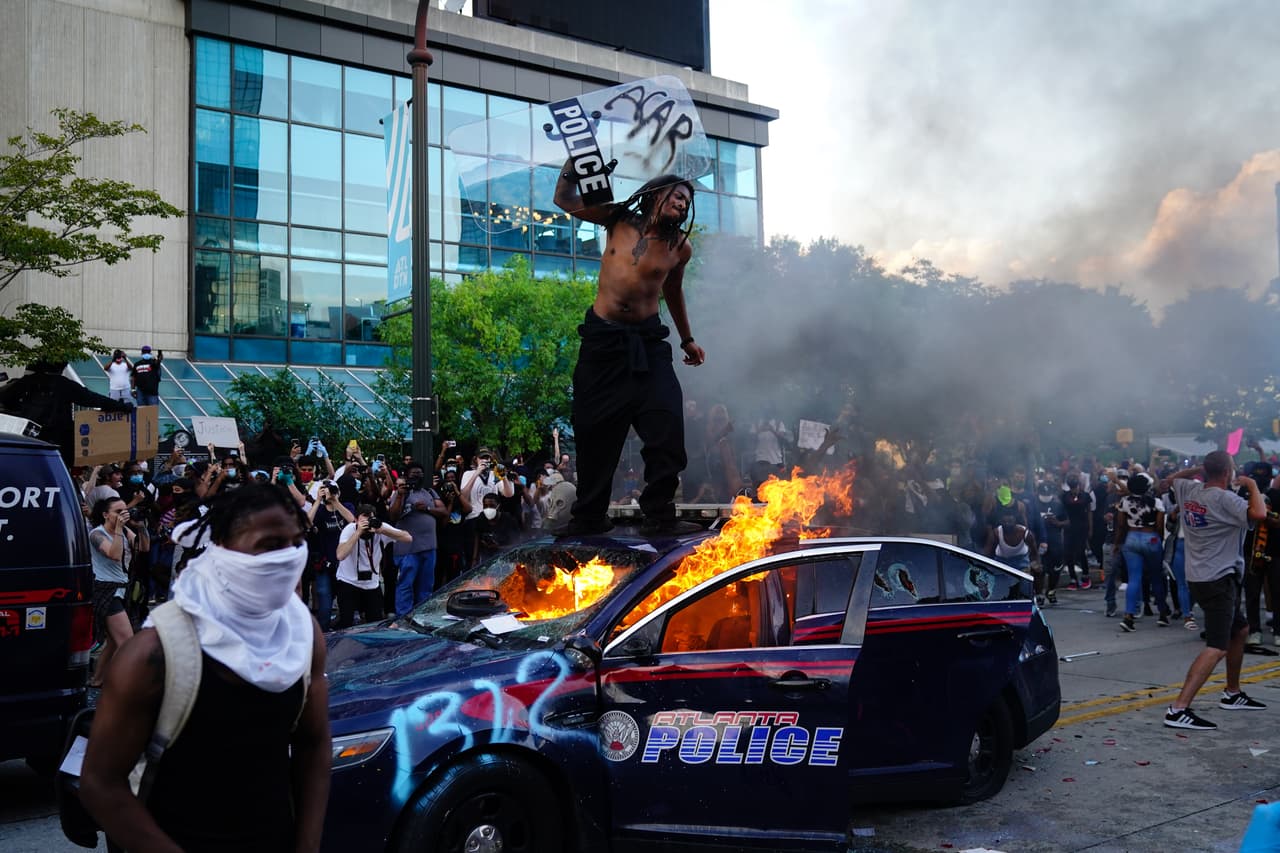 Un hombre se para encima de una patrulla de la Policía de en llamas durante una protesta el 29 de mayo de 2020 en Atlanta, Georgia.