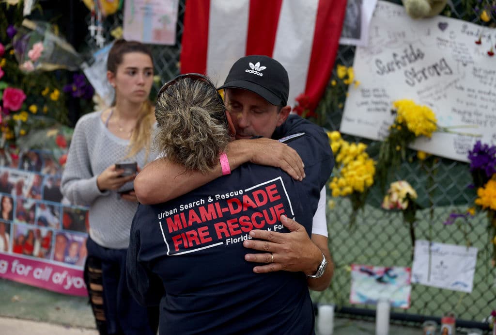 La bombera Maggie Castro abraza a Pablo Langesfeld mientras visitan el monumento a las víctimas en el condominio Champlain Towers South. La hija del señor Langesfeld, Nicole Langesfeld, es una de las desaparecidas tras 
<a href="https://www.univision.com/temas/derrumbe-de-edificio-en-surfside-miami">el colapso del edificio de Surfside</a>.