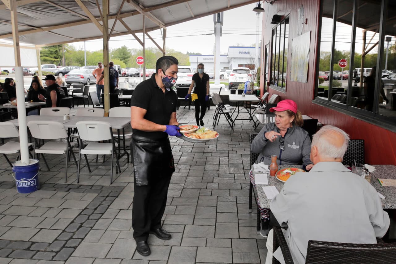 Un mesero enmascarado sirve a los clientes de un restaurante en Manchester, New Hampshire. El local se mantenía cerrado desde marzo pero el 18 de mayo comenzó a atender a las personas en el área al aire libre.