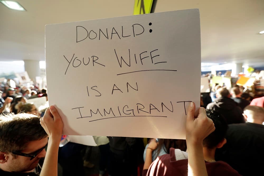 Una persona levanta un cartel donde se lee "Donald: tu mujer es una inmigrante" en San Francisco International Airport
