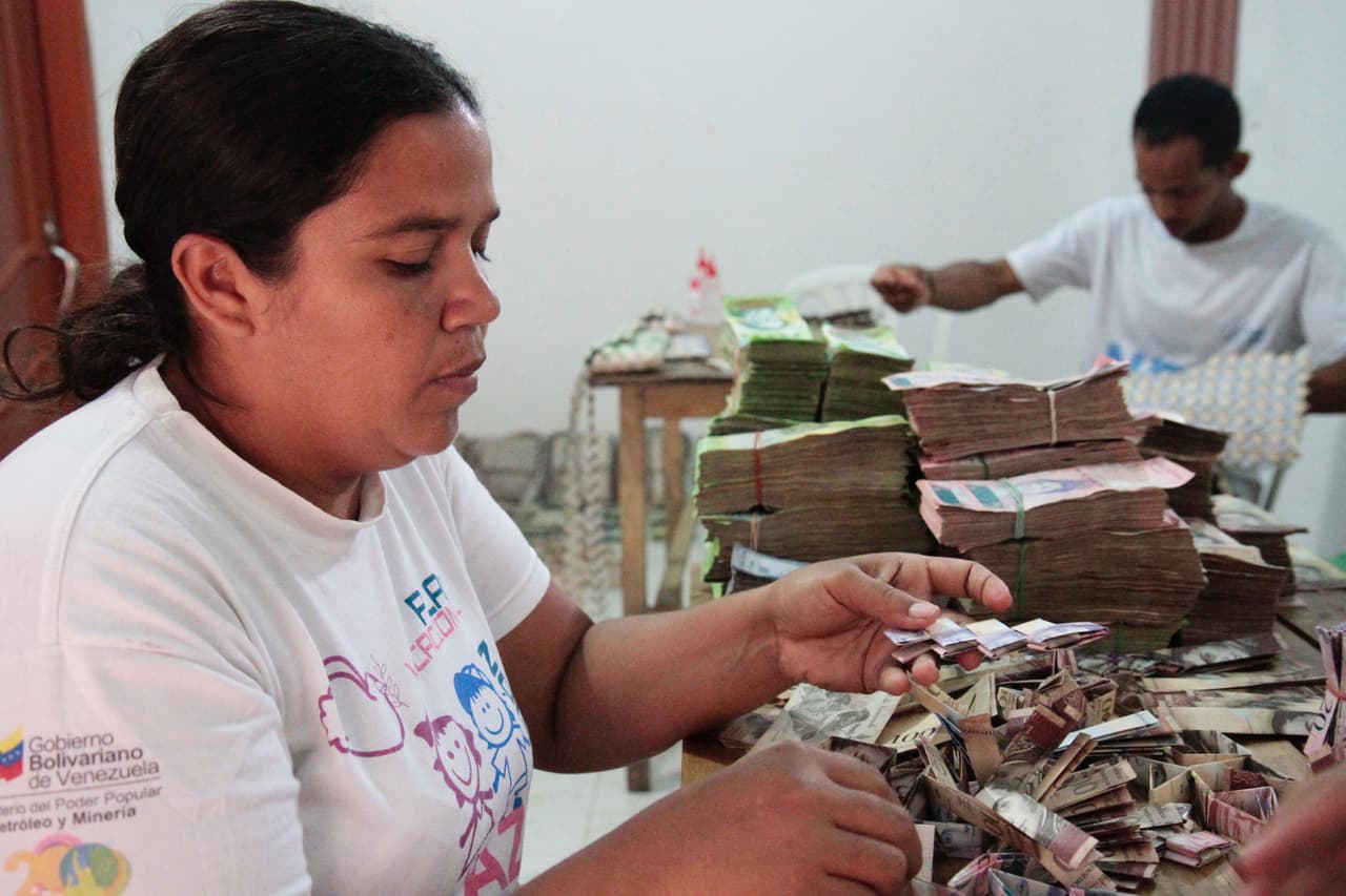Para ganarse la vida, la pareja trabaja largas horas elaborando bolsos hecho de billetes de bolivares. En su país natal, la hiperinflación ha disparado los precios y ha hecho que el dinero pierda capacidad de compra. Un café vale ya 200,000 bolívares en las panaderías de Caracas y un kilo de pollo sobrepasa el millón de bolívares.