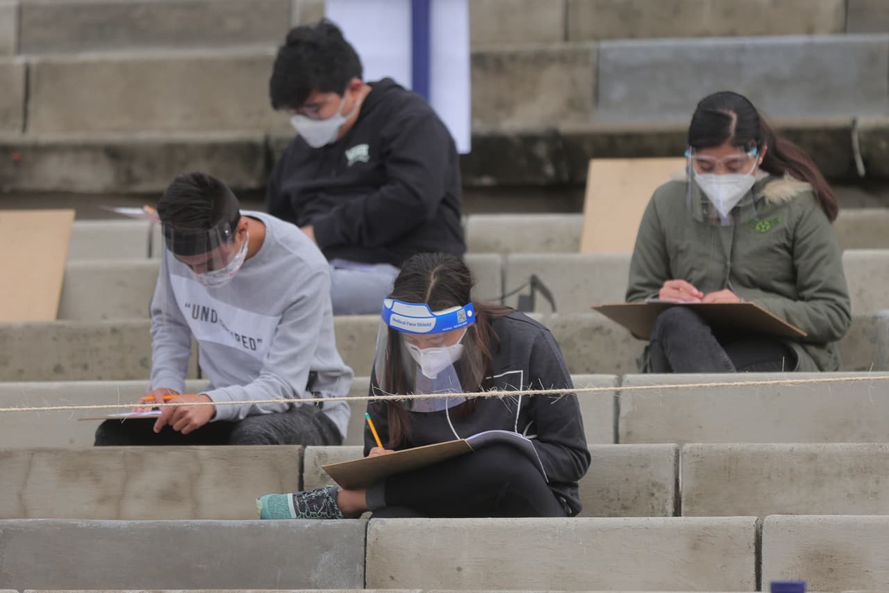 Alumnos toman el examen de admisión en las gradas mientras siguen las medidas preventivas para evitar el Covid-19, como la distancia entre sí. 
<b>La escena se convirtió en algo rudimentario, debido a que cada aspirante colocó una tabla sobre sus rodillas y llenó una copia en papel del examen, que contiene 120 preguntas. </b>Los estudiantes estarán en vilo hasta que se publiquen los resultados el 21 de septiembre.
<br>
<br>