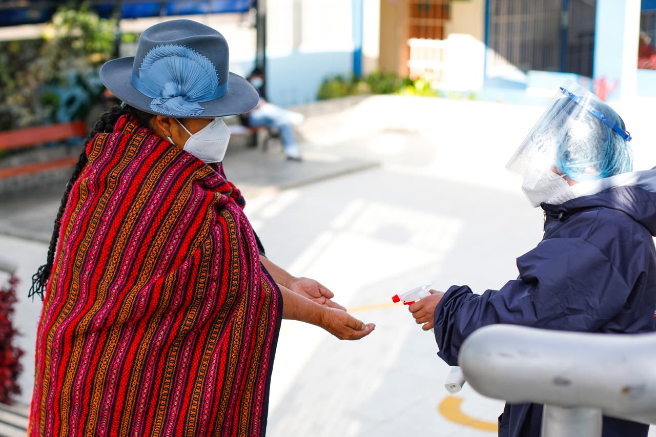 En Perú, los votantes acudieron a las urnas para elegir entre 
<b><a href="https://www.univision.com/noticias/america-latina/quienes-son-los-favoritos-en-las-elecciones-presidenciales-en-peru">18 candidatos, </a> lo practicamente garantizaba una segunda vuelta. </b>En la imagen, una representante de la Oficina Nacional de Procesos Electorales (ONPE) rocía alcohol en las manos de una votante a la entrada de un centro.