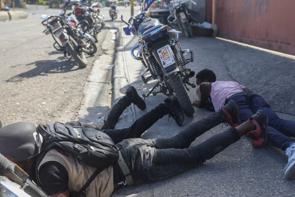 Personas se cubren en medio de un intercambio de disparos entre pandillas y policías en Puerto Príncipe (AP Photo/Odelyn Joseph)