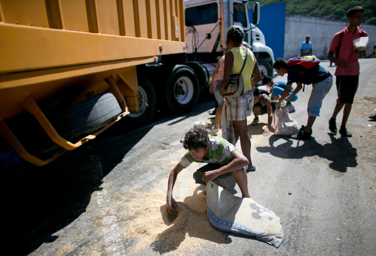 Un joven utiliza una funda de almohada para recoger arroz del pavimento caído de un camión de mercancías que espera para entrar en Puerto Cabello, la ciudad portuaria por la que pasan la mayoría de importaciones de alimentos del país.
