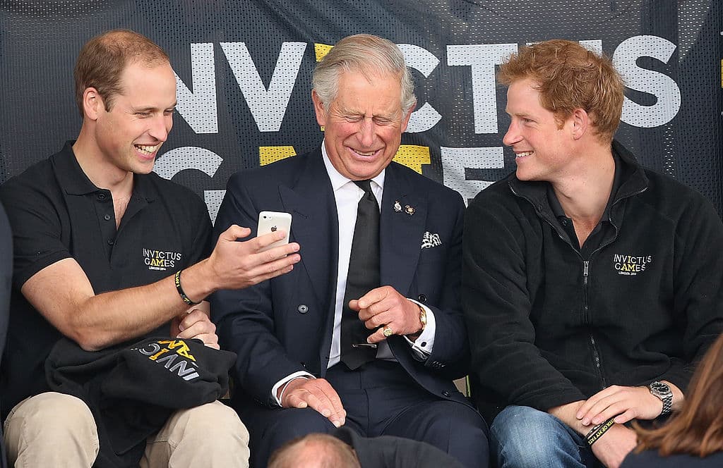 El Príncipe Guillermo, el Príncipe Harry y el Príncipe Carlos miran un teléfono móvil mientras observan el atletismo en la pista de Lee Valley durante los Juegos Invictus el 11 de septiembre de 2014 en Londres, Inglaterra.