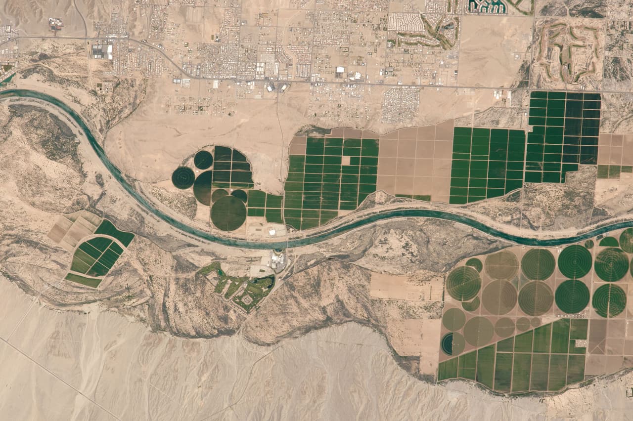 Mirando hacia abajo en las vistas del desierto del suroeste de Estados Unidos, un astronauta tomó esta fotografía de una sección corta del río Colorado. Este alcance del río está marcado por campos agrícolas de tonos oscuros, rectangulares y redondos, restringidos a la estrecha zona de tierra cultivable en la llanura aluvial cerca del río.