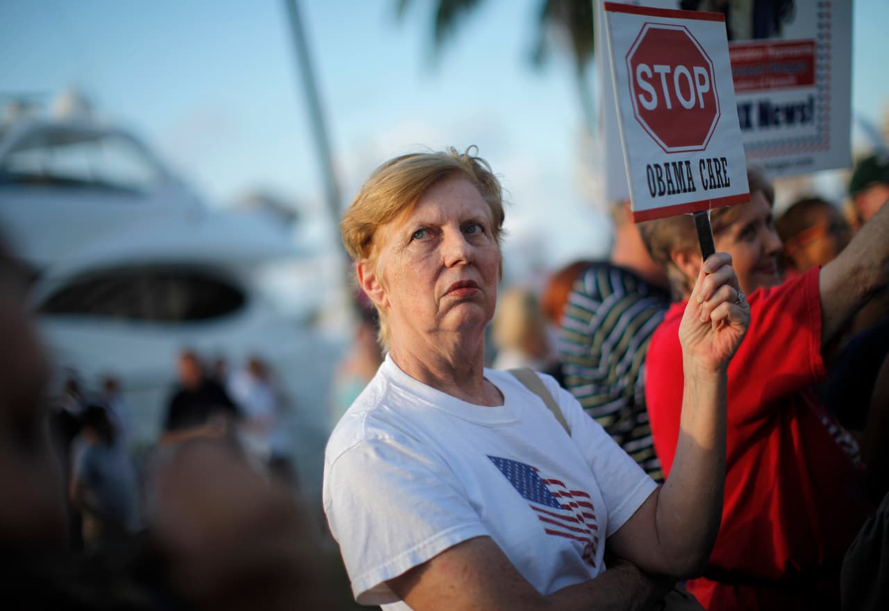 Una residente del sur de Florida sostiene una pancarta en protesta a la reforma sanitaria de Obama en Miami, Florida, en octubre de 2009. Siete años después el aumento del costo de las primas, especialmente en estados como Arizona, ha generado especiales críticas entre sus detractores. Otro de los aspectos que genera polémica desde su aprobación es 
<b>el requisito en la ley de que la mayoría de los estadounidenses contrate un seguro de salud o afrontará multas</b>. Pero esa, explican sus defensores, es la única manera de balancear el mercado entre sanos y enfermos.