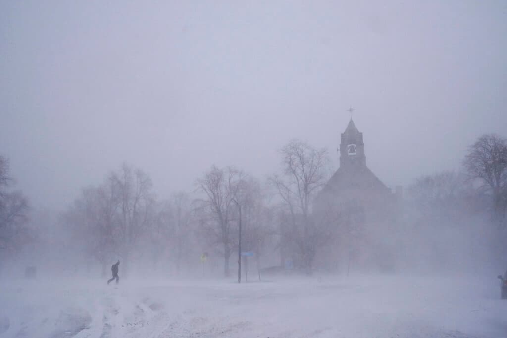 Un peatón con equipo para la nieve avanza por el Colonial Circle, con la silueta de la iglesia episcopaliana de St. John's Grace entre la ventisca, en Buffalo, Nueva York, el sábado 24 de diciembre de 2022.
