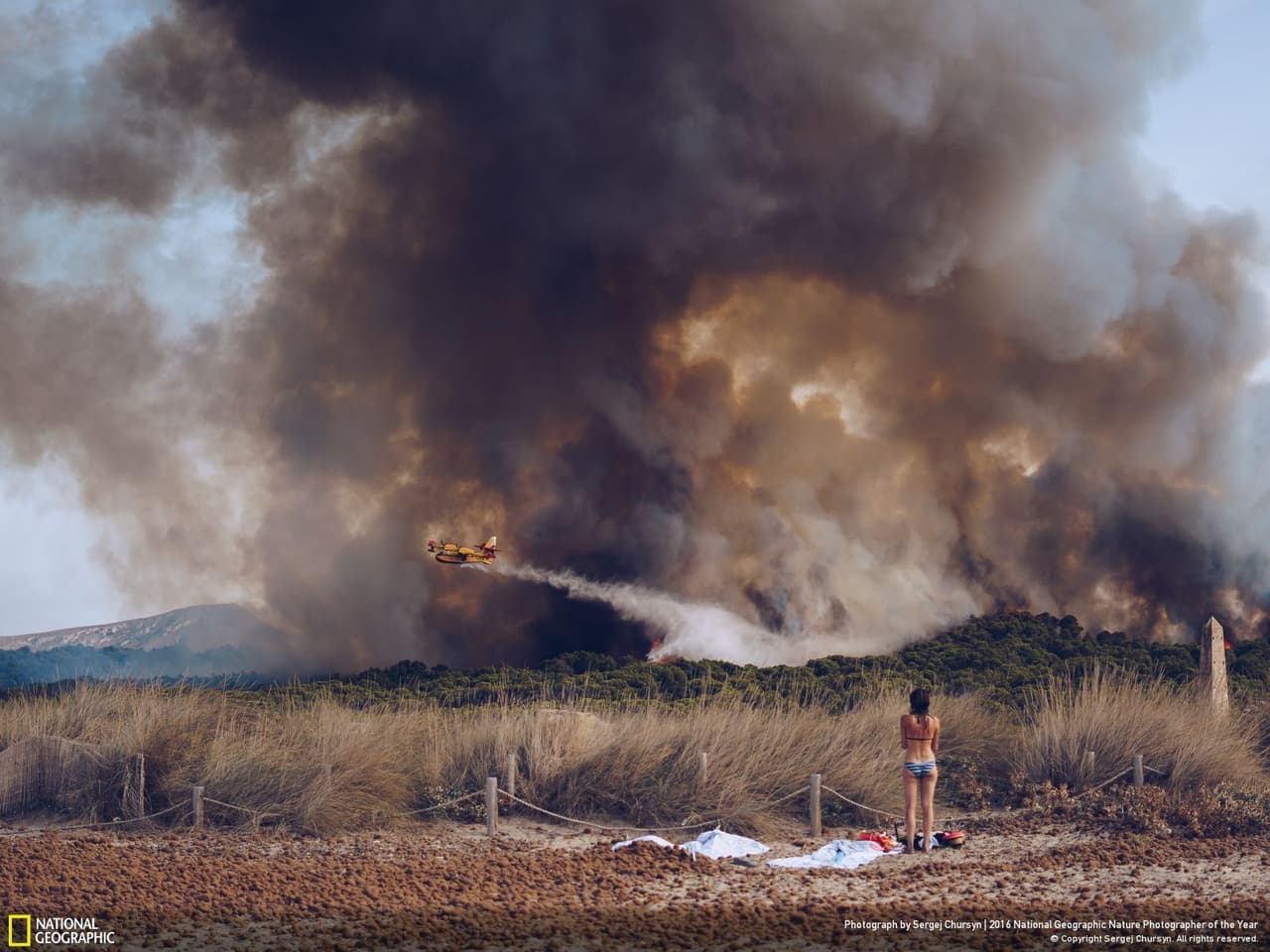 Una mujer observa desde la playa Son Serra un incendio forestal que destruye un bosque en la isla de Mallorca. La foto tomada por Sergej Chursyn obtuvo una mención honorífica en asuntos medioambientales.