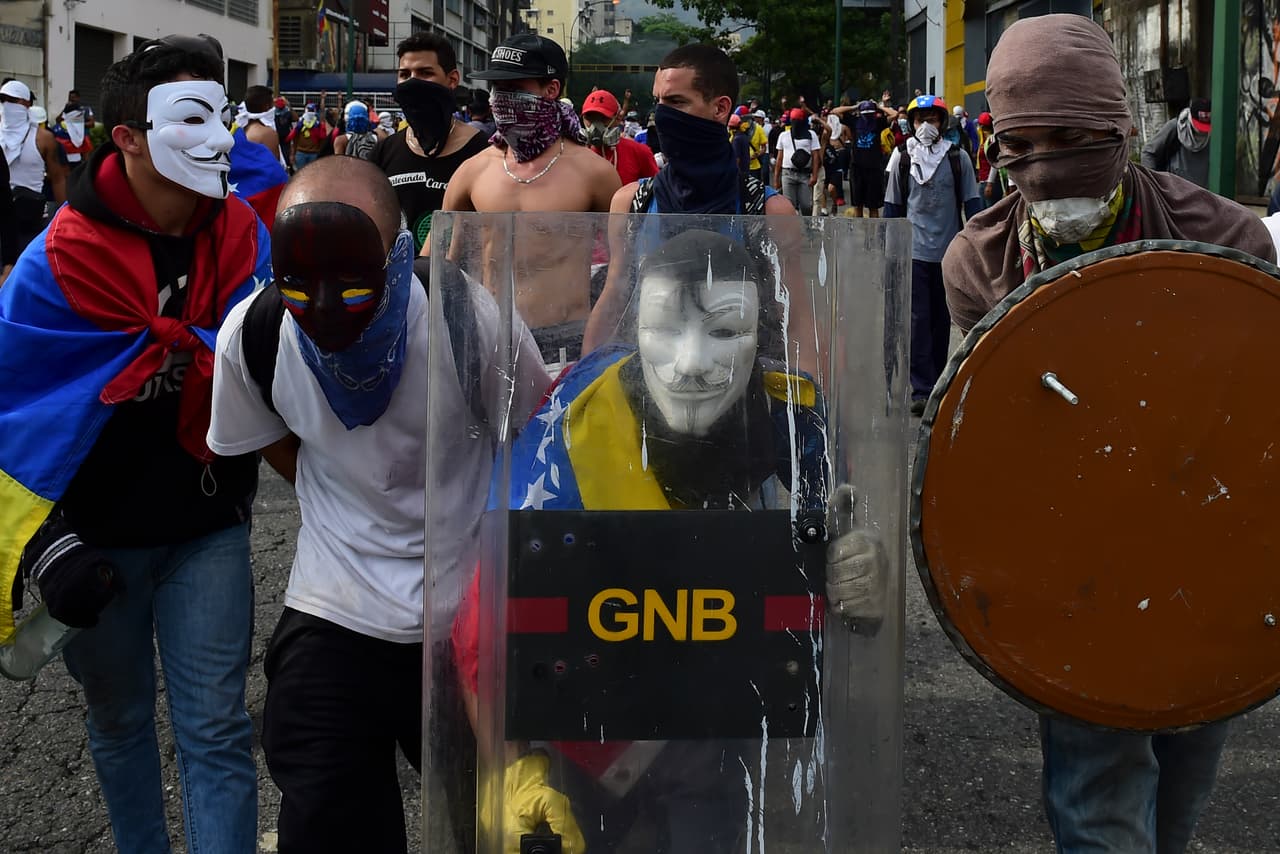 Un opositor enmascarado lleva un escudo que tomó de la Guardia Nacional Bolivariana.