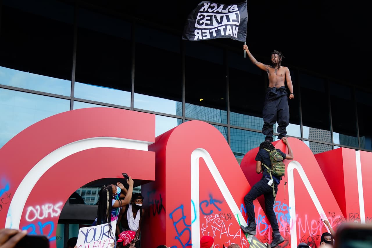 Un hombre agita una bandera de Black Lives Matter sobre el emblema CNN durante una protesta en respuesta al asesinato policial de George Floyd frente al Centro CNN el 29 de mayo de 2020 en Atlanta, Georgia.
