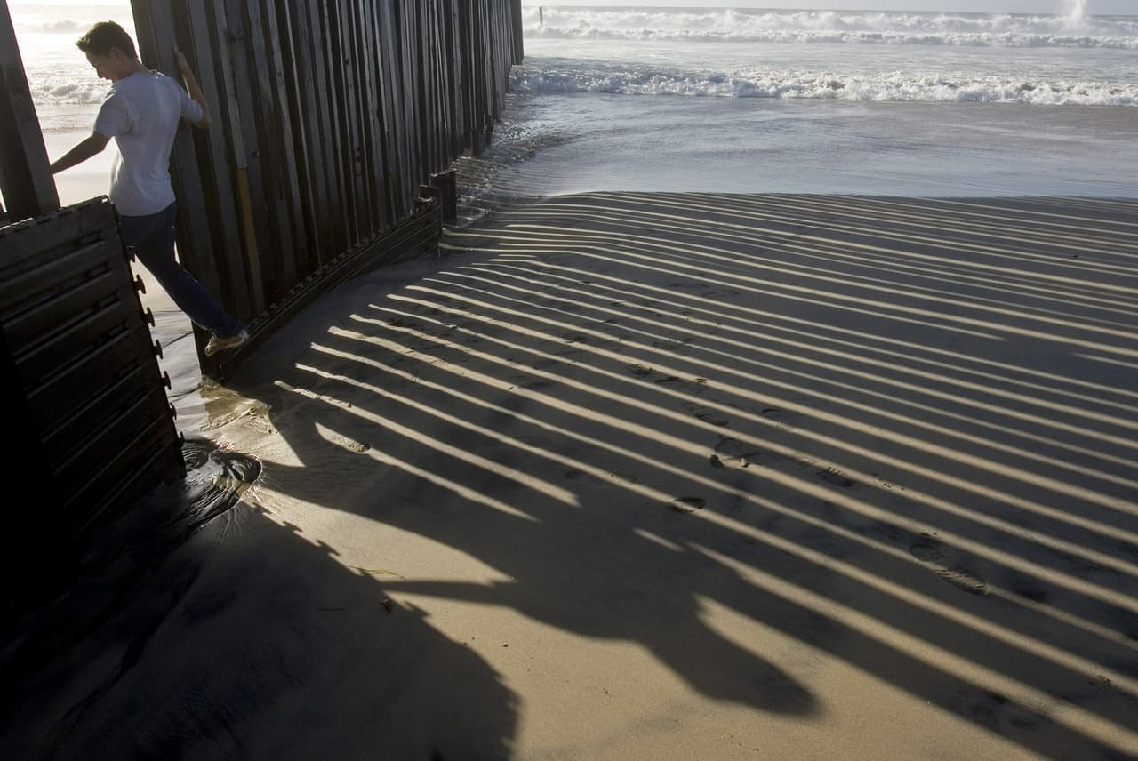 Un hombre cruza de regreso a México por una abertura de la valla en la playa de San Diego, luego que una tormenta causara daños a la estructura el 3 de enero de 2006. Las barreras han sido construidas con diferentes estilos y materiales: muros para peatones edificados con planchas metálicas, otros con malla reforzada y unos más con tubos de acero de cinco centímetros de diámetro colocados uno al lado del otro. Algunas zonas solo tienen vallas contra vehículos, unas barreras metálicas de corta altura que no impiden el paso de peatones pero sí imposibilitan el cruce de automóviles.