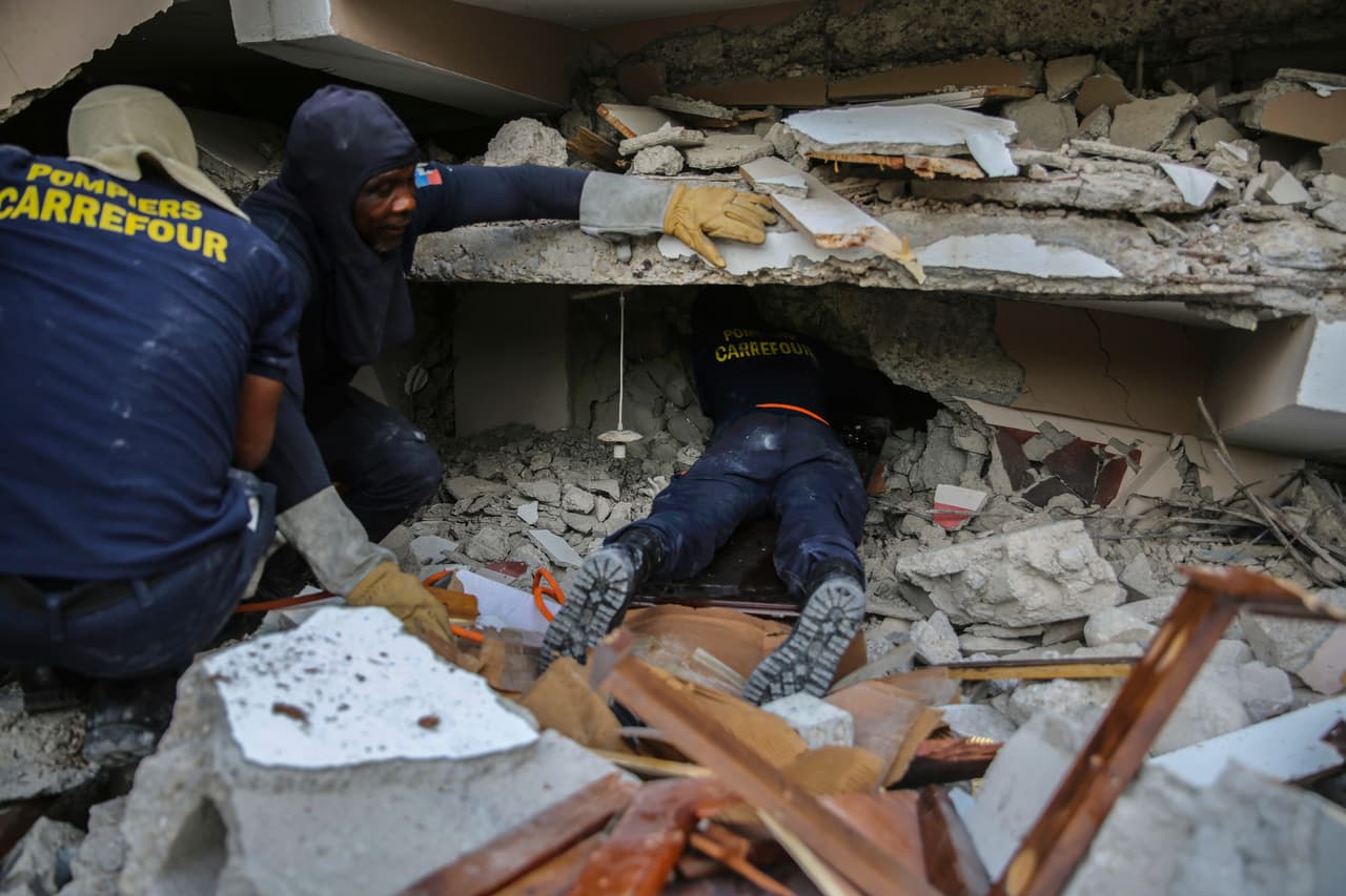 Bomberos buscan entre los escombros en un edificio colapsado en Les Cayes.