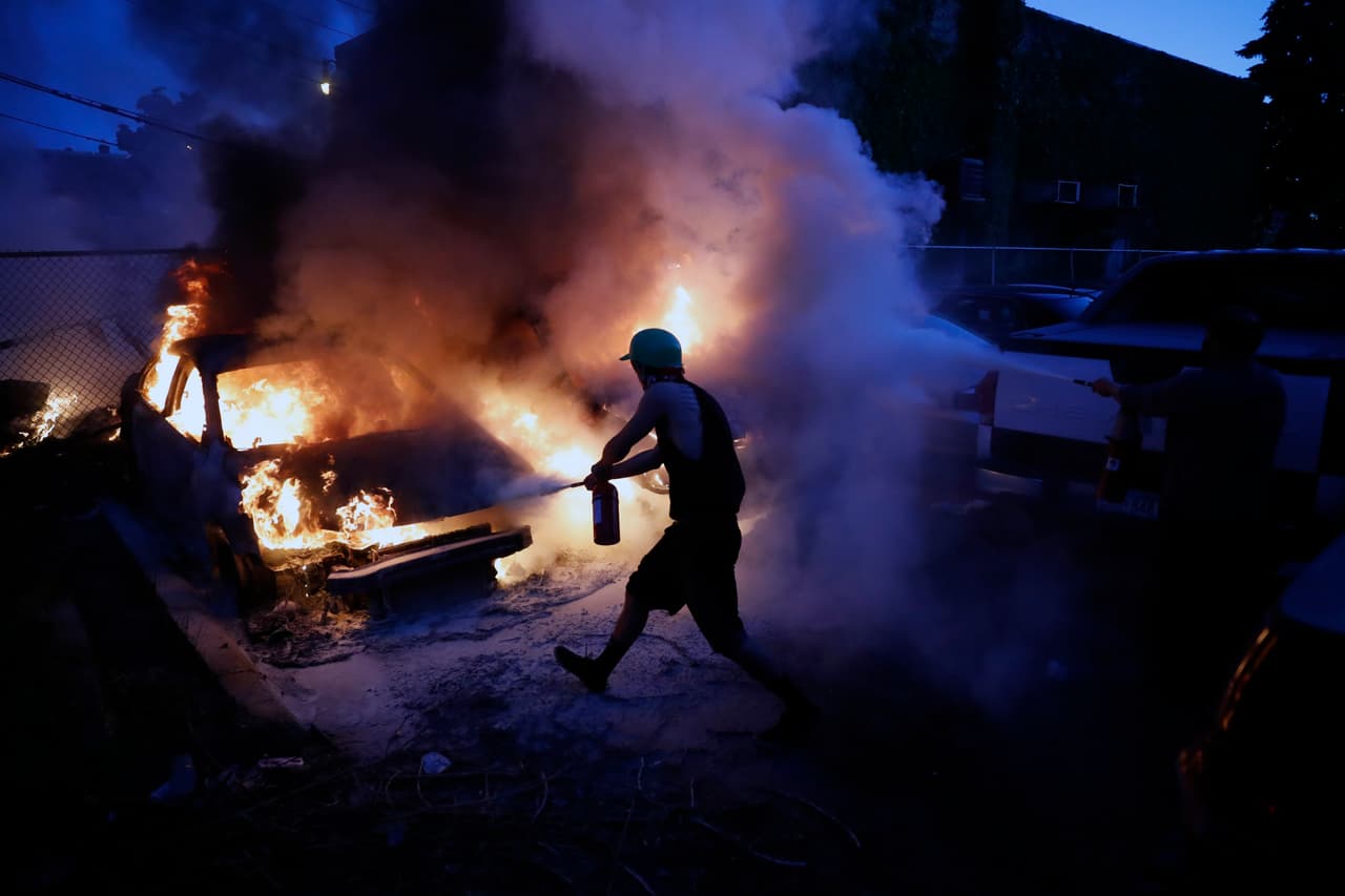 Hacia la noche, las acciones vandálicas y actos violentos comienzan a extenderse en Minneapolis y otras ciudades. En la imagen, un hombre intenta extinguir los automóviles en llamas.