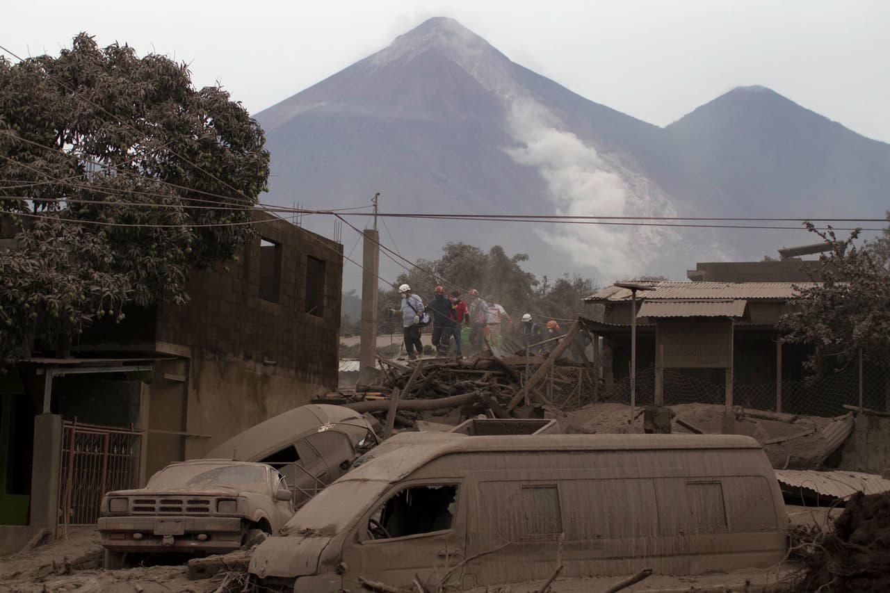 Rescatistan buscan sobrevivientes en Escuintla, al fondo el cráter humeante del volcán.