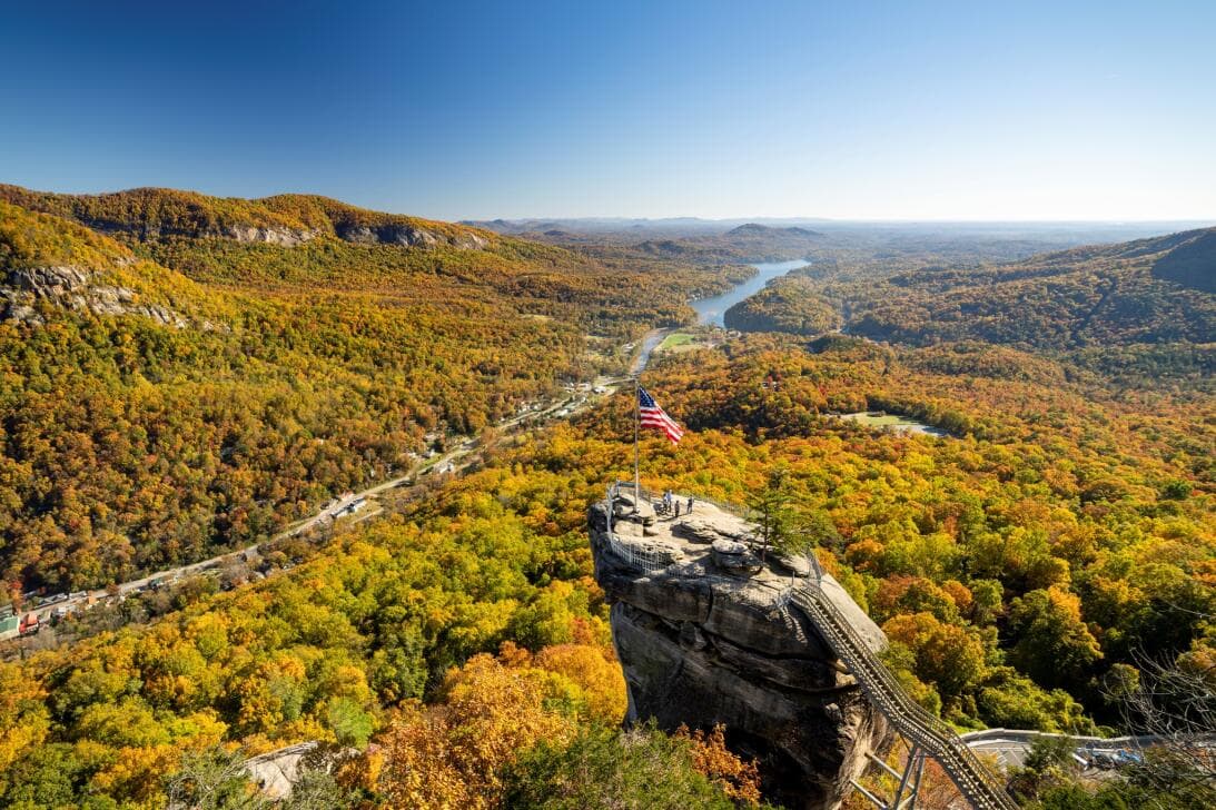 <b>OTOÑO (Inicia oficialmente el 22 de septiembre de 2024):</b>
<br>
<br>El otoño es la temporada favorita para muchos debido al cambio de color del follaje. Uno de los puntos más impresionantes para apreciar este espectáculo es 
<b>Chimney Rock State Park</b>. El histórico parque abarca casi 7,000 acres y ofrece impresionantes vistas del follaje de otoño. Por supuesto, la mejor vista es desde la cima de Chimney Rock, un monolito de granito de más de 500 millones de años y 315 pies de altura. Desde lo alto se puede ver el lago Lure y numerosas cadenas montañosas a lo largo del horizonte.