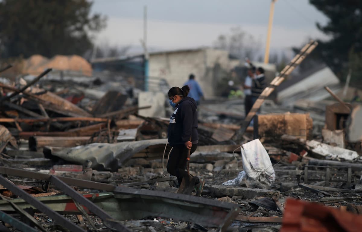 Una mujer con tapaboca rebusca entre los escombros del incendio