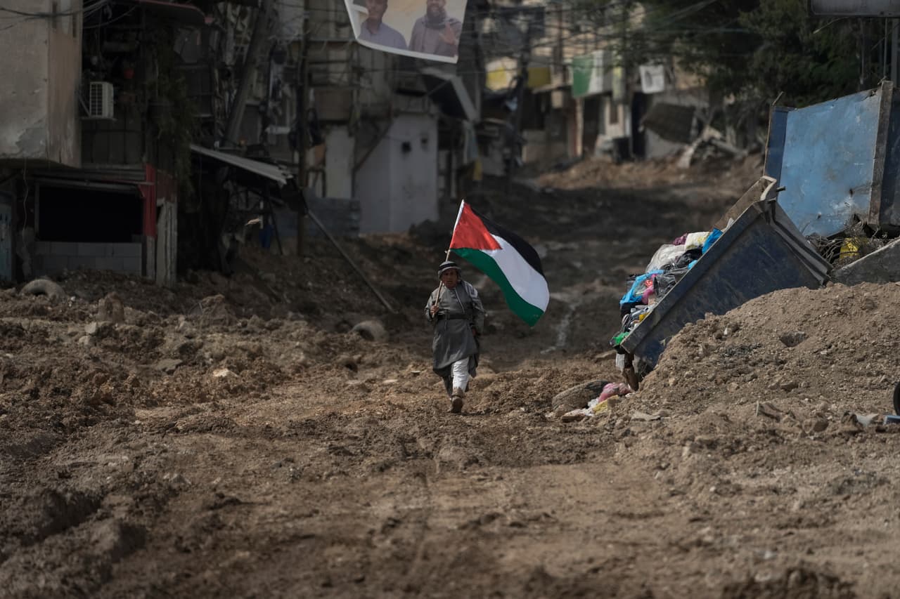 El activista palestino Khairi Hanoon camina con la bandera de Palestina en medio de un camino arruinado luego del paso de las 
<a href="https://www.univision.com/noticias/mundo/israel-guerra-en-gaza-transformacion-de-israel-en-un-estado-paria-analisis-luciano-zaccara">tropas israelíes en Tulkarem, Cisjordania,</a> en septiembre de 2024. La violencia de la guerra en Gaza se extendió por el otro territorio palestino ocupado, que no está gobernado por Hamas, sino por la Autoridad Palestina.