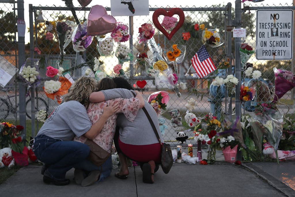 Tres personas se abrazan frente al memorial de la escuela secundaria Marjory Stoneman Douglas en Parkland, Florida, tras el tiroteo que dejó 17 muertos en febrero de 2018.