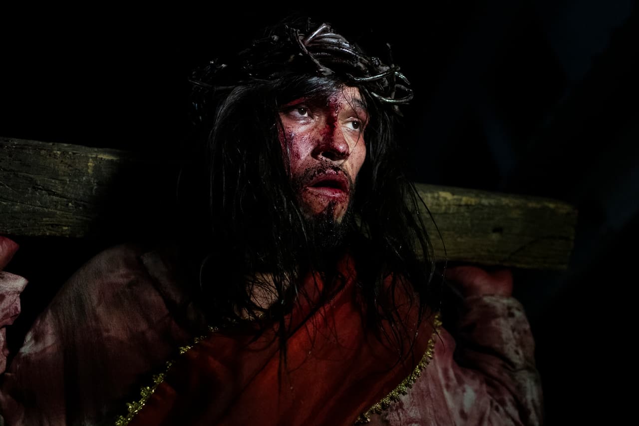 Luiz Henrique, interpretando a Jesucristo, carga una cruz durante una representación del Vía Crucis como parte de las celebraciones de Semana Santa, en la favela Complexo do Alemão en Río de Janeiro, el Viernes Santo, 18 de abril de 2025. 
<br>