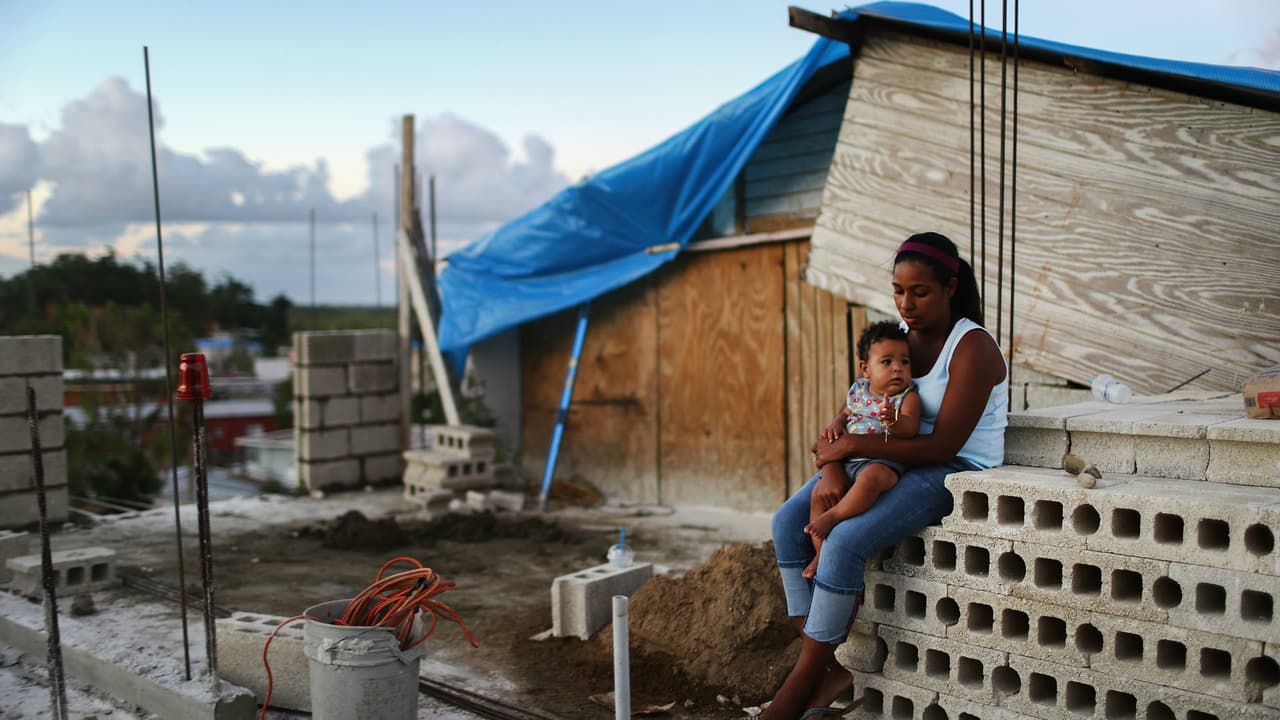 Una mujer con su bebé frente a su hogar dañado por el huracán María en Puerto Rico.