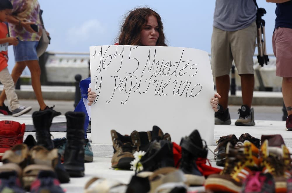 Entre los ciudadanos que acudieron al acto de este viernes figuran Cristina Vázquez O'Neill, quien se ubicó frente a los zapatos con un cartel que leía "4,645 muertos y mi papá fue uno de ellos".