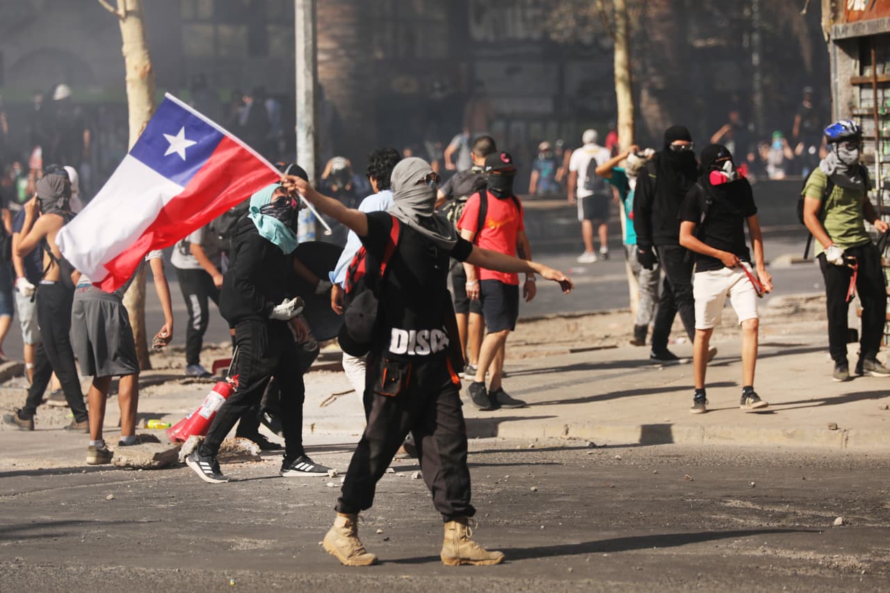 Si bien el alza en el precio del metro fue el detonante de las protestas que se han prolongado por casi dos meses, los jóvenes chilenos han salido a las calles a 
<b>exigir mejores pensiones, sueldos "dignos" y "educación de calidad</b>", uno de los grandes reclamos históricos de los estudiantes. En la foto, un joven manifestante ondea una bandera chilena en el Día de los Derechos Humanos, el 10 de diciembre del 2019, en Santiago. Tanto 
<b>Human Rights Watch como Amnistía Internacional han advertido sobre violaciones a los derechos humanos</b> por parte de la policía y los militares.