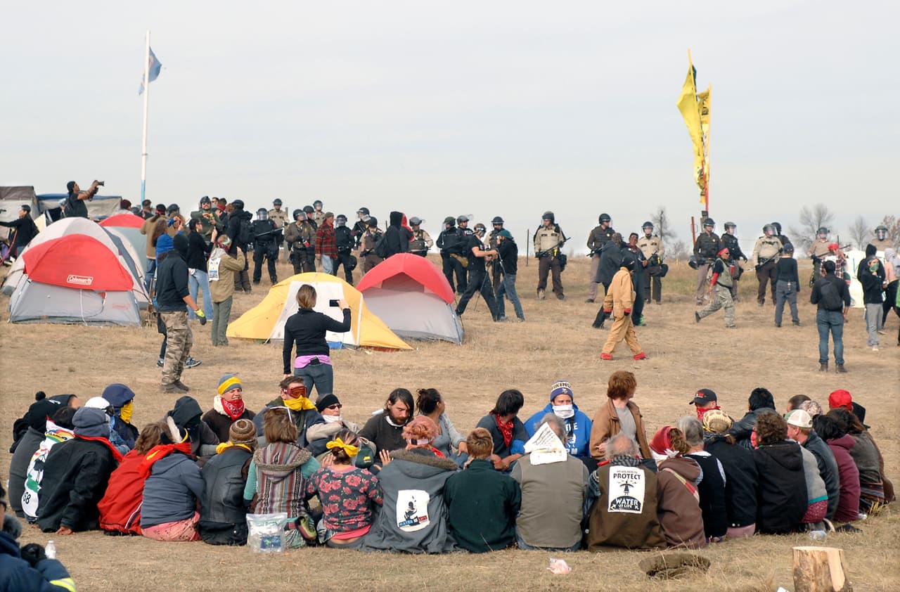Los manifestantes sentados en círculo rodeados de agentes de seguridad en Sacred Stones