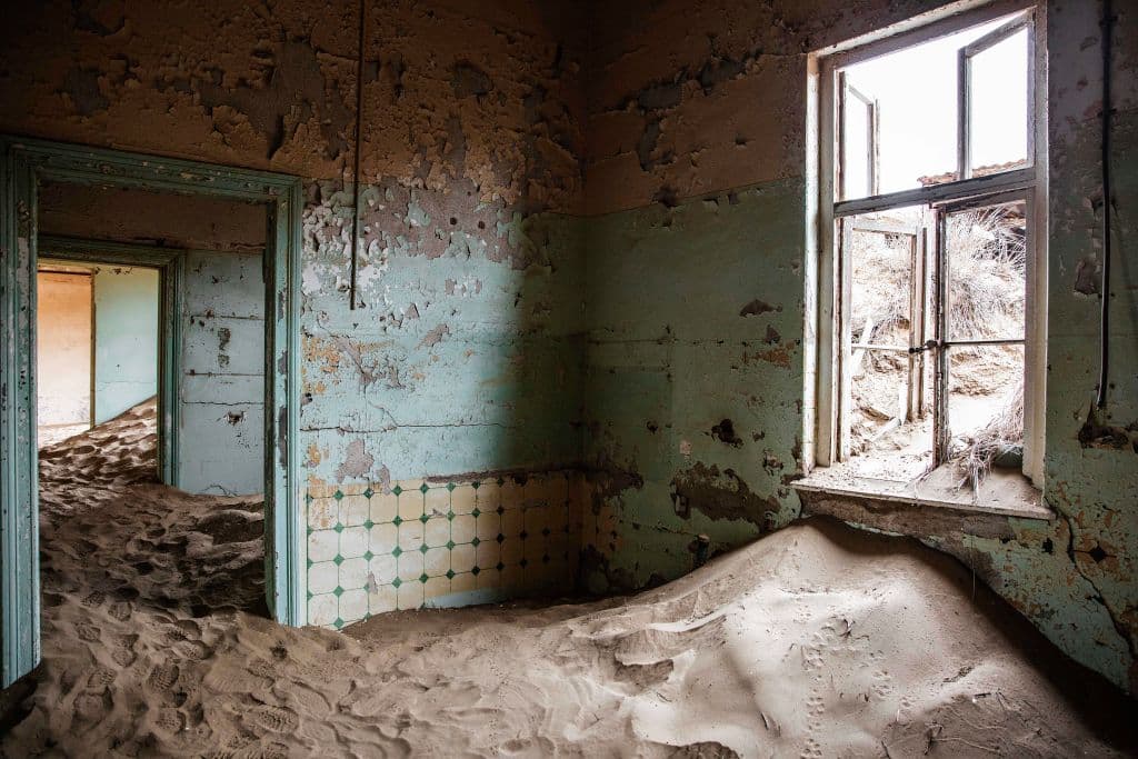 <b>Kolmanskop, Namibia.</b> A inicios del siglo XX, trabajadores alemanes hallaron que esta área de Lüderitz era rica en diamantes. 
<b>Poco a poco se fueron asentando obreros y mineros que levantaron un pueblo arquitectónicamente alemán. </b>El próspero asentamiento llegó a tener tranvía, hospital y sala de juegos. Pero con el agotamiento de la mina, el pueblo fue quedándose vacío hasta finalmente volverse fantasma en los años 50. 
<b>Por las fuerzas naturales del desierto de Namibia, Kolmanskop se fue cubriendo de arena y hoy sus edificios se entremezclan con médanos, volviéndose un fotogénico destino. </b>
<br>
<br>
<br>
