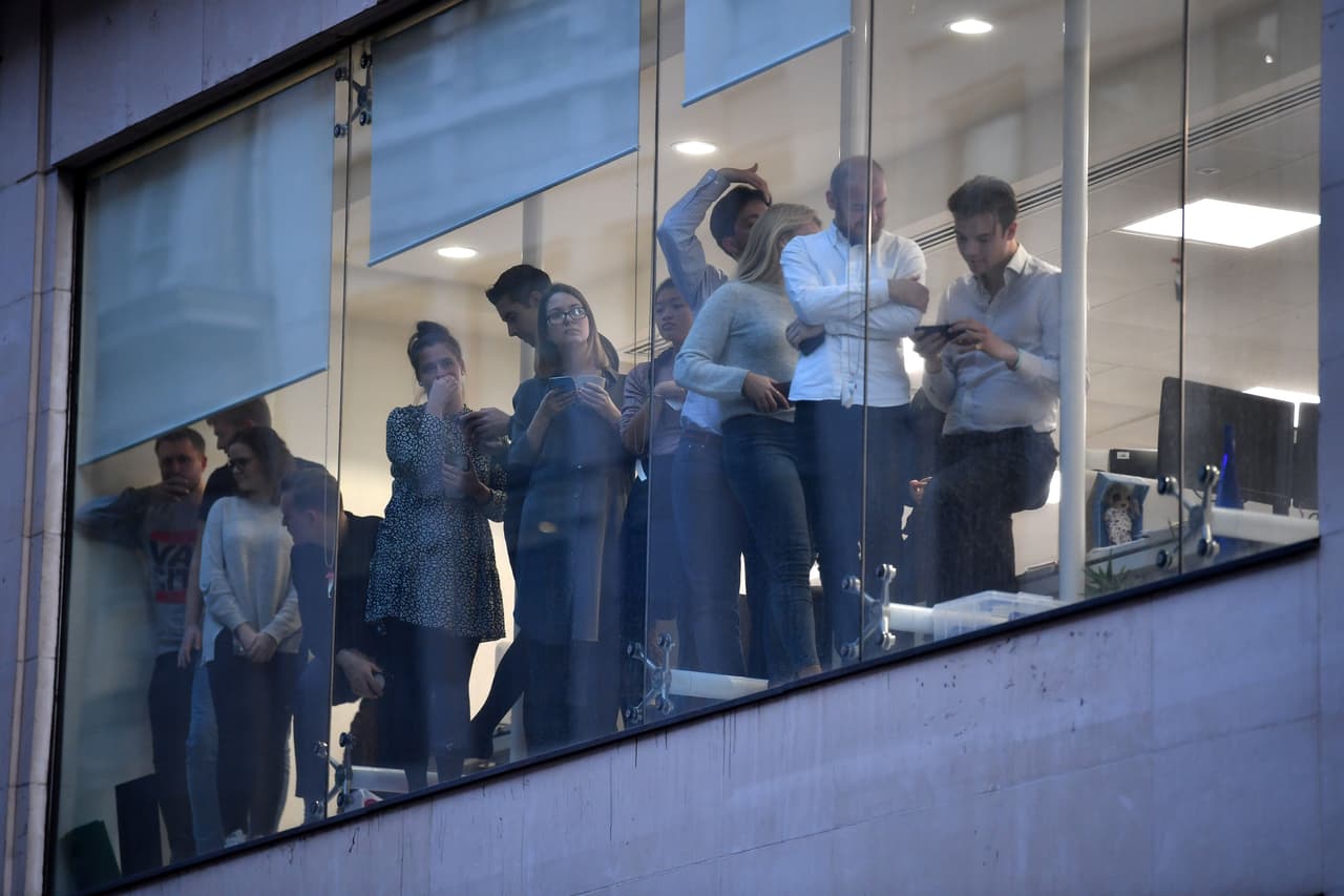 Trabajadores del área se asoman a las ventanas que dan al mercado Leadenhall, cerca del puente de Londres en el centro de la ciudad.