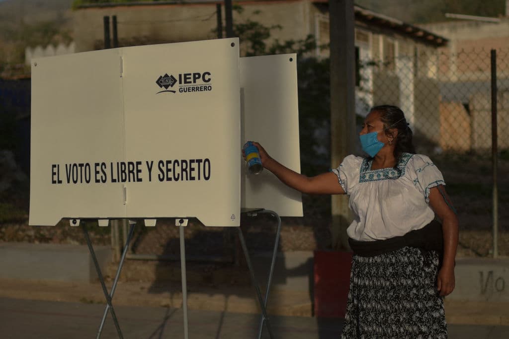 Una integrante de una casilla electoral desinfecta una cabina de votación. La pandemia también ha marcado estas elecciones y ha dificultado su organización. El uso de mascarillas es obligatorio en los recintos y a quien no la lleve se le entregará una para entrar.