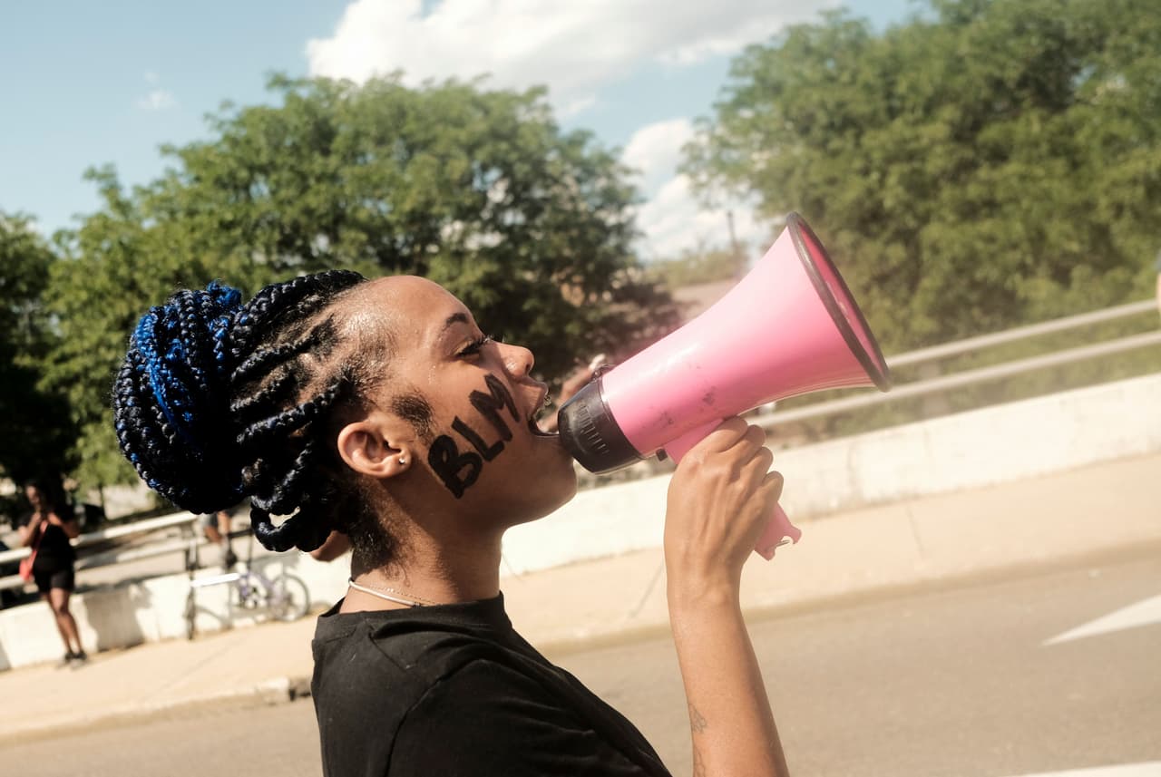 Una mujer con la cara pintada con las siglas BLM (Black Lives Matter) protesta gritando a través de un megáfono a la multitud en las afueras del ayuntamiento de Akron. Los agentes hallaron una pistola, un cargador y un anillo de bodas en el asiento del automóvil que conducía Walker, y más tarde se encontró un casquillo que coincidía con el arma que los oficiales creían que se había disparado en su contra desde el vehículo.