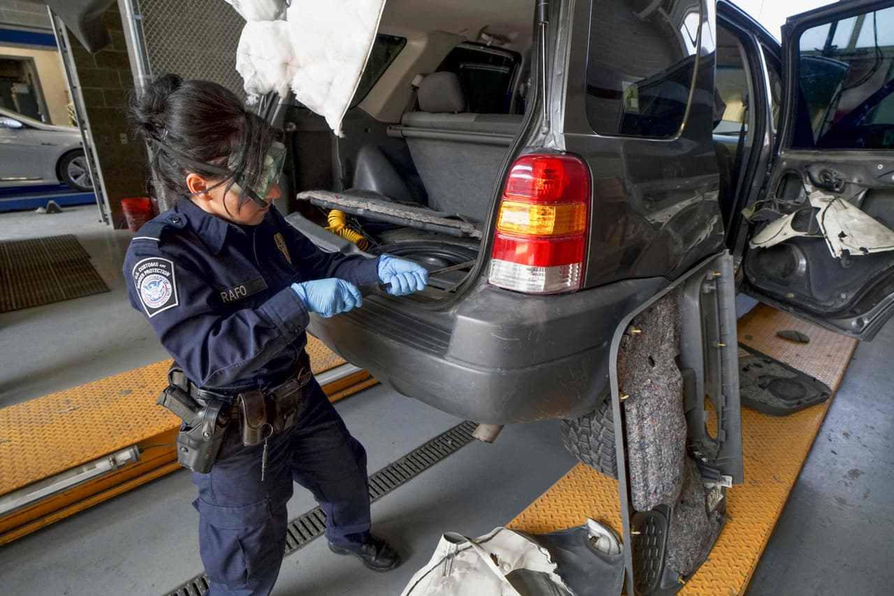 Una agente aduanal busca droga en una camioneta SUV.