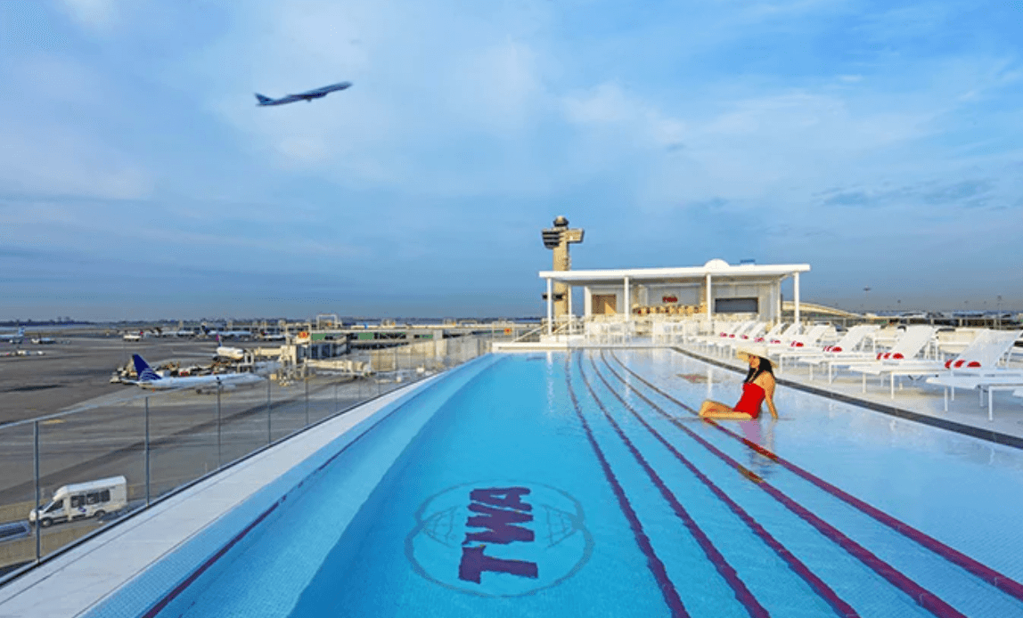 <b>TWA Hotel</b>
<br>Uno Idlewild Drive
<br>Aeropuerto Internacional JFK
<br>Queens, Nueva York
<br>
<a href="https://www.google.com/search?q=twa+hotel+address&rlz=1C5GCEM_enUS990US990&oq=twa+hotel+address&aqs=chrome.0.0i457i512j46i20i175i199i263i512j0i512l5j0i10i512j0i512.3160j0j4&sourceid=chrome&ie=UTF-8">(212) 806-9000</a>
<br>
<br>
<b>Esta piscina infinita </b>(con el agua al nivel de sus muros para que se desborde) es toda una piscina ‘de altura’ pues queda en la azotea del TWA Hotel. Y, como está en el aeropuerto JFK, desde ella puedes disfrutar de las emocionantes vistas de la pista 4 izquierda/22 derecha de JFK.
<br>
<br>Pero ni te creas que tienes que hospedarte en el hotel para nadar en ella: acepta reservaciones a partir de las 11h y sus precios son asequibles: $25 de lunes a jueves y $50 de viernes a domingo. Las reservaciones se hacen en: poolbar@twahotel.com y duran solo 1.45 horas. 
<br>