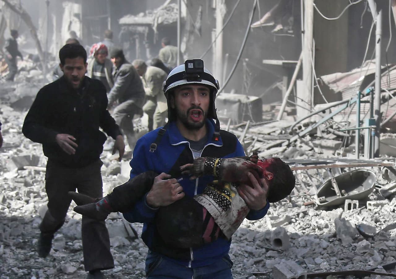 19 de febrero. Un miembro de la defensa civil siria lleva a un niño herido rescatado de entre los escombros de los edificios después del bombardeo del gobierno en Hamouria. Este día, cuando 127 civiles murieron, fue 
<a href="https://www.reuters.com/article/us-mideast-crisis-syria-ghouta/more-bombs-hit-syrias-ghouta-death-toll-highest-since-2013-idUSKCN1G40N8">el mayor número de víctimas mortales en un solo ataque desde 2013</a>.