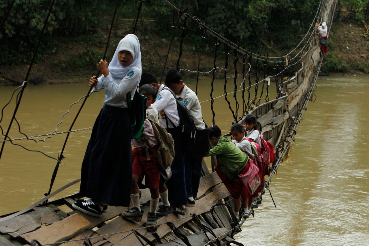 <b>Indonesia.</b> Estudiantes se aferran a las barras laterales de acero de un puente colapsado para cruzar un río y llegar a la escuela en la aldea de Sanghiang Tanjung, luego de severas inundaciones. 19 de enero de 2012. 
<br>