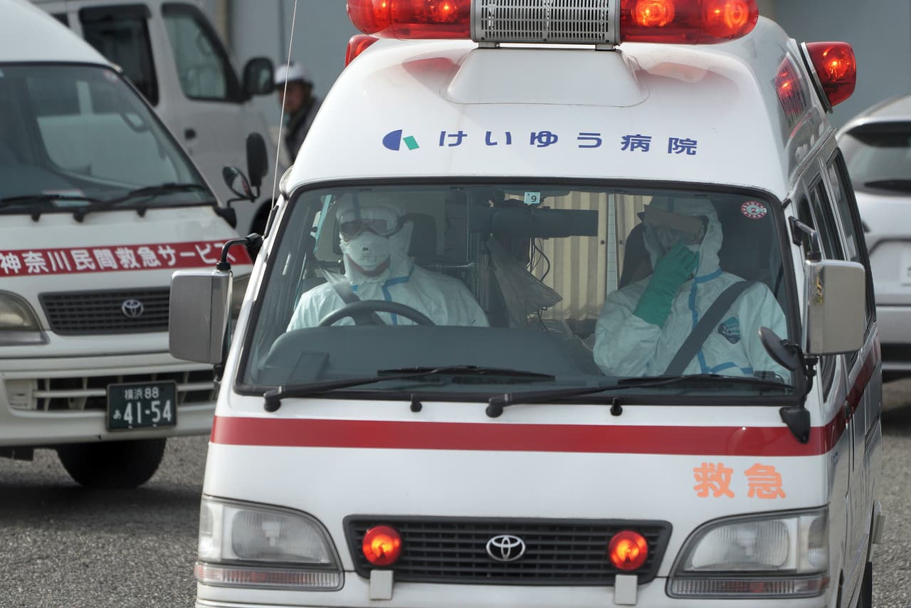 Oficiales en trajes protectores conducen una ambulancia cerca del crucero Diamond Princess anclado en el puerto de Yokohama. La situación especial con este crucero podría prolongarse hasta dos semanas.