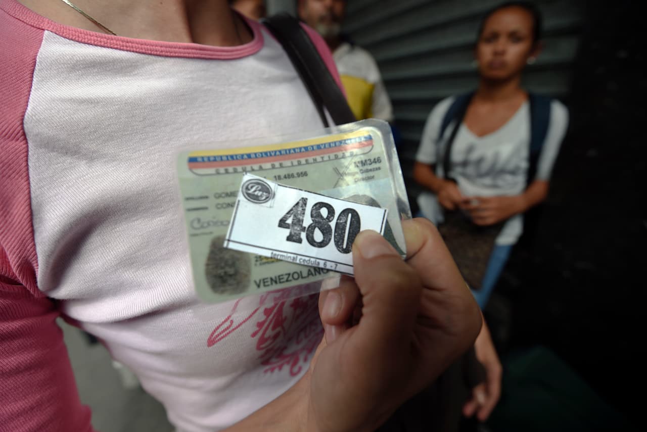 Según la encuestadora Datanálisis, en febrero de 2016 la escasez de productos en los comercios de Caracas fue de 82,3%. A cada ciudadano le corresponde un día determinado de la semana para hacer la fila y poder comprar los alimentos disponibles. Quien no quiere pasar horas de espera puede ir al mercado negro que multiplica el precio. En la foto, una mujer muestra su número en la fila para comprar comida.