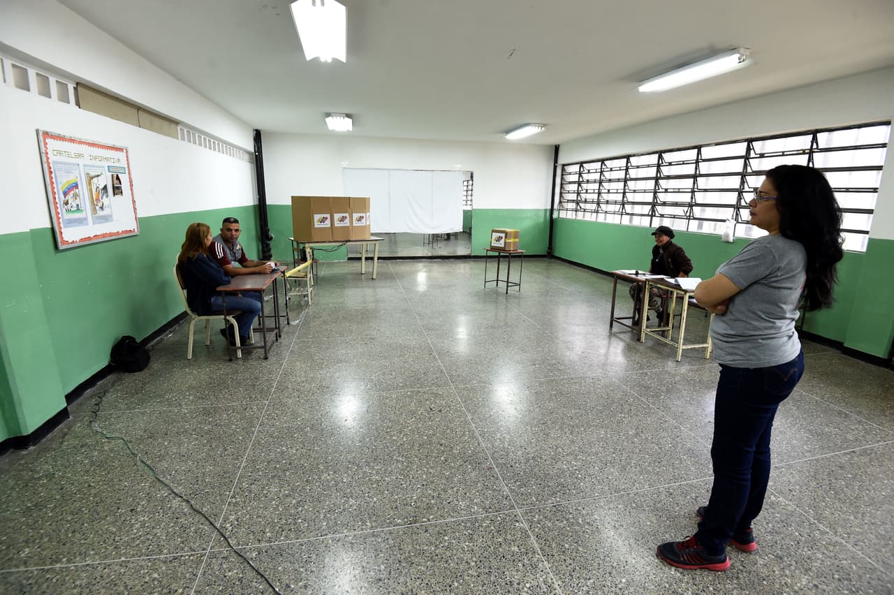Funcionarios del Consejo Nacional Electoral (CNE) esperan en un salón de clases vacío, habilitado como centro votación.