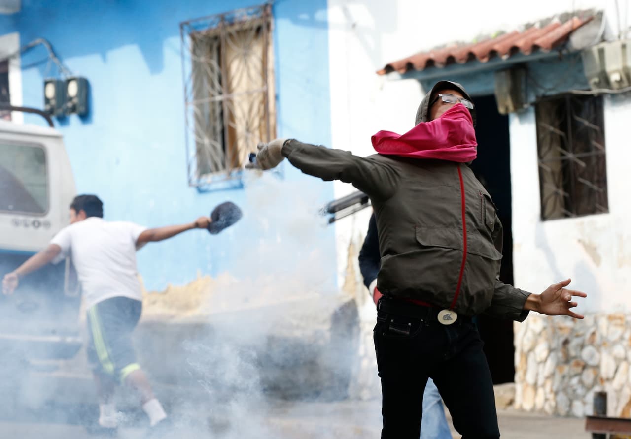 Un opositor al gobierno de Maduro lanza un objeto contra las fuerzas de seguridad que reprimen a los vecinos de la barriada popular.