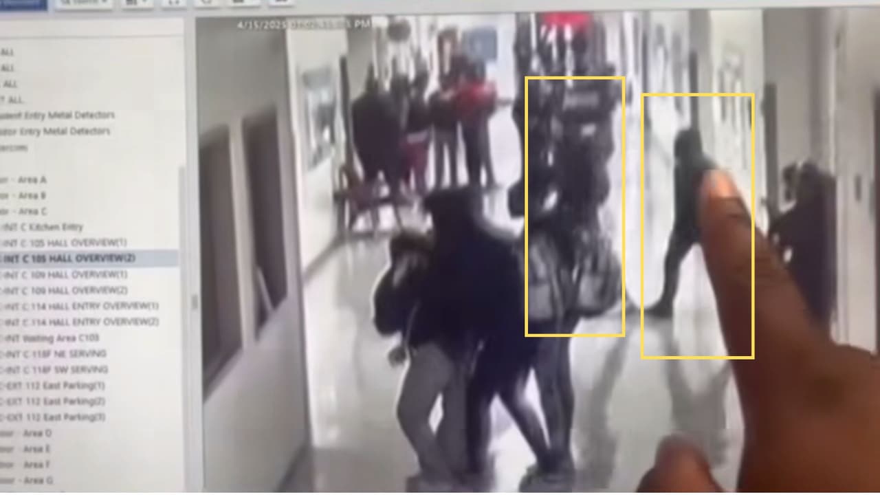 La persona mantiene el dedo sobre la pantalla mientras señala cómo el joven, que 
<b>parece llevar parte de la cabeza cubierta con la capucha de una sudadera o chamarra</b>, cruza el pasillo entre los alumnos, al tiempo que 
<b>otro joven camina en la misma dirección, de frente a él.</b>