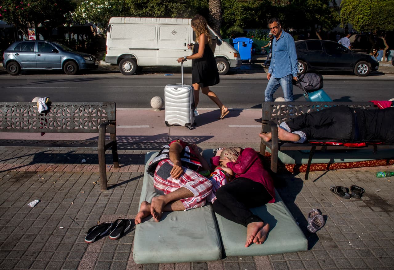 <b>Capítulo 2. “No hay cielo ni tierra cuando te hundes en el mar”. </b>El mundo de los turistas y de los refugiados apenas coincide en el tiempo y en los lugares. La mayoría de los botes desembarcan al amanecer cuando los turistas todavía duermen en sus hoteles y los refugiados duermen en la calle, lo más cerca posible de la comisaría. Suelen coincidir en el puerto del ferry, pero los oficiales de la Autoridad Portuaria desalojan a gritos y con porra en mano a los que osan dormir en la zona o intentar fotografiar la escena 
<b><a href="http://huelladigital.univisionnoticias.com/crisis-refugiados-javier-bauluz/capitulo-2/">(VER ESPECIAL COMPLETO).</a></b>