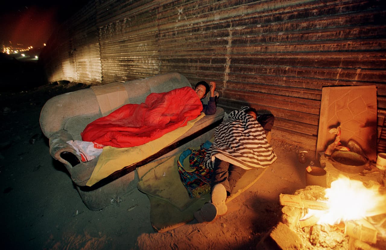 Two Mexican migrants lie next to a fire for warmth in the freezing Tijuana night, waiting for the right moment to jump over the border fence into California in this photo taken November 26, 2000. 1.5 million illegal immigrants are caught annually by U.S. border patrol agents in this region alone. Mexican President-elect Vicente Fox, who will be sworn in on December 1, has appointed a border tsar to focus on better treatment of migrants by the United States. DA/RCS - RTRBGX9