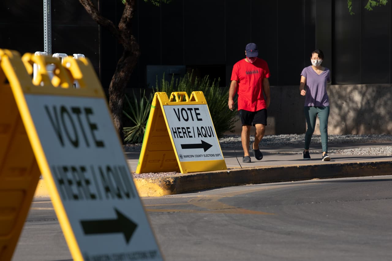Dos personas usando máscaras salen de uno de los centros de votación del condado Maricopa. De acuerdo con la oficina de registro al inicio de la mañana el sitio web con la información de los lugares para votar estuvo caído pero el problema fue solucionado rapidamente.