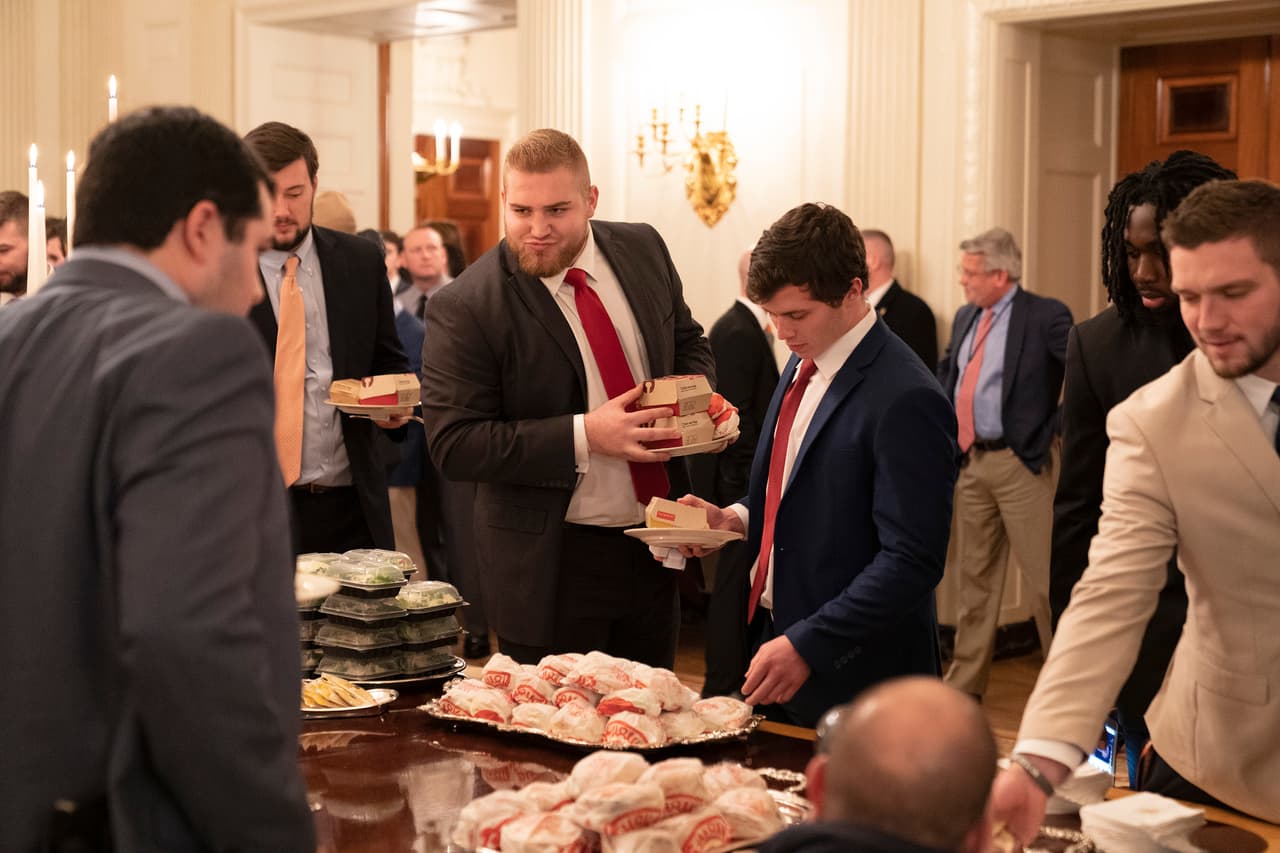 Después de las palabras de Trump, los jugadores, vestidos con trajes elegantes, llenaron sus platos con los particulares manjares.