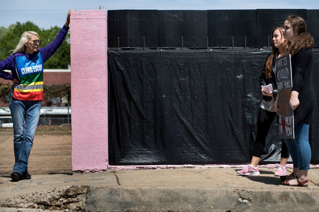 La escena es del pasado mes de abril. A la izquierda, una voluntaria viste un chaleco con las palabras: "Escolta de la clínica". Su trabajo es acompañar a las pacientes que acuden a la única clínica que ofrece abortos en Mississippi. A la derecha, activistas antiaborto.