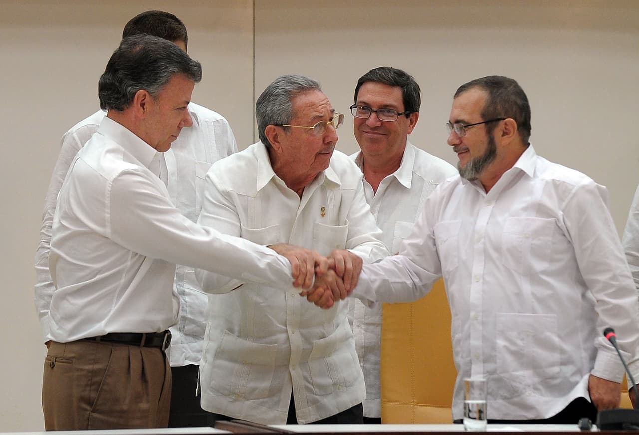 <b>La esperanza del fin del conflicto en La Habana.</b> Luego de más de cuatro intensos años de negociación, en agosto de 2016 llegan a un acuerdo que pone fin a 52 años de conflicto. En la fotografía, Alias Timochenko, líder del grupo guerrillero despúes de varias sucesiones, aprieta la mano de Santos durante uno de los encuentros de los diálogos de paz en La Habana. En el centro, el entonces presidente de la isla, Raúl Castro.