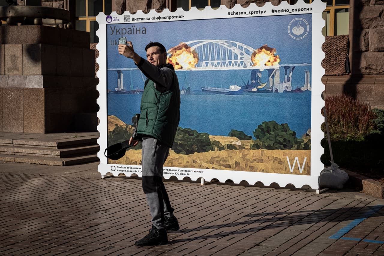 La gente posa para fotografías frente a una imagen de un sello postal. 
<b>En las últimas semanas, Ucrania ha logrado avances significativos en el este y el sur del país, recuperando áreas que estuvieron en manos de Rusia.</b>
<br>
<br>Algunos funcionarios ucranianos celebraron la explosión del puente de Crimea aunque no llegaron a reclamar responsabilidad. El servicio postal ucraniano anunció que emitiría sellos que conmemoran la explosiónpara resaltar el "significado sagrado" del puente para Moscú.