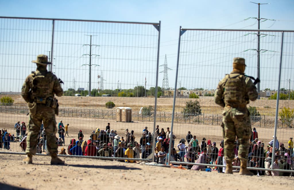 Migrantes esperan junto a una valla fronteriza mientras son vigilados por miembros de la Guardia Nacional de Texas, para ingresar a El Paso, Texas. La Patrulla Fronteriza detuvo a cerca de 10,000 personas el martes, una de las cifras más altas para un solo día, según un funcionario federal citado por la AP. Más de 27,000 personas se encontraban en custodia. La cifra de personas en custodia varían a medida que los migrantes son liberados o deportados, pero en marzo había 8,600 personas en esta condición.
